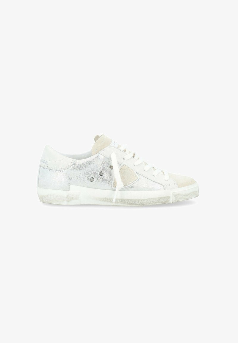 Sneaker bianco con accenti metallici argento, sovrapposizioni in suede e occhielli circolari. Lacci piatti e suola testurizzata per una migliore aderenza.