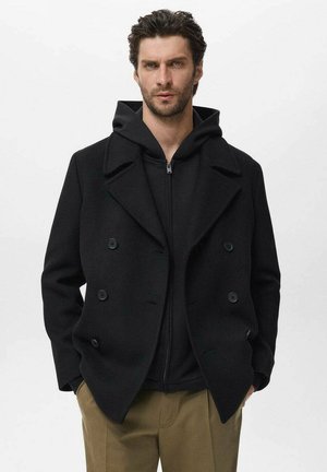 Black double-breasted wool coat with large lapels, paired with a black zip-up hoodie, worn over beige trousers. Smooth texture, no visible patterns.