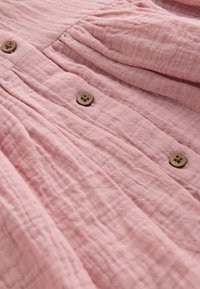 Weicher rosa gekräuselter Stoff mit vertikal angeordneten Holzknöpfen, der Falten und Plissees nahe der Oberseite zeigt.