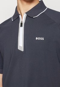 Polo bleu marine en mélange de coton avec un col à zip, un passepoil blanc et un logo sur le devant. Manches courtes avec une coupe classique.