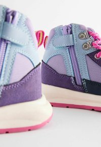Baskets violettes et bleues avec des textures en maille et en daim, dotées de lacets roses, de fermetures éclair et d'une semelle blanche avec des accents roses.