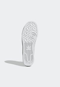White sneaker sole with a textured pattern, featuring circular and diamond shapes. Branding on the heel and intricate tread design for grip.