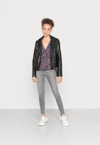 Giubbotto motociclistico in pelle nera sopra una blusa floreale blu navy e rosa, abbinato a jeans skinny grigi chiari e sneakers bianche.