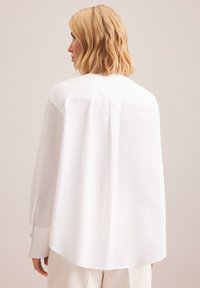 Camicia bianca a maniche lunghe con una vestibilità comoda, dotata di una piega sul retro, orlo arrotondato e polsini abbottonati. Tessuto morbido e leggero.
