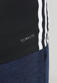 Top atlético negro con textura acanalada, que presenta tres franjas blancas a los lados y un logo "CLIMALITE" cerca del dobladillo.