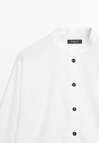 Chemise blanche à manches longues avec col mao et quatre boutons foncés sur le devant, étiquetée Massimo Dutti.