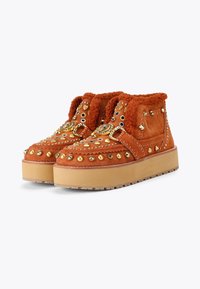 Pomarańczowe zamszowe botki na platformie z teksturowanym wykończeniem, zdobione metalowymi ćwiekami i okrągłymi elementami na cholewce.