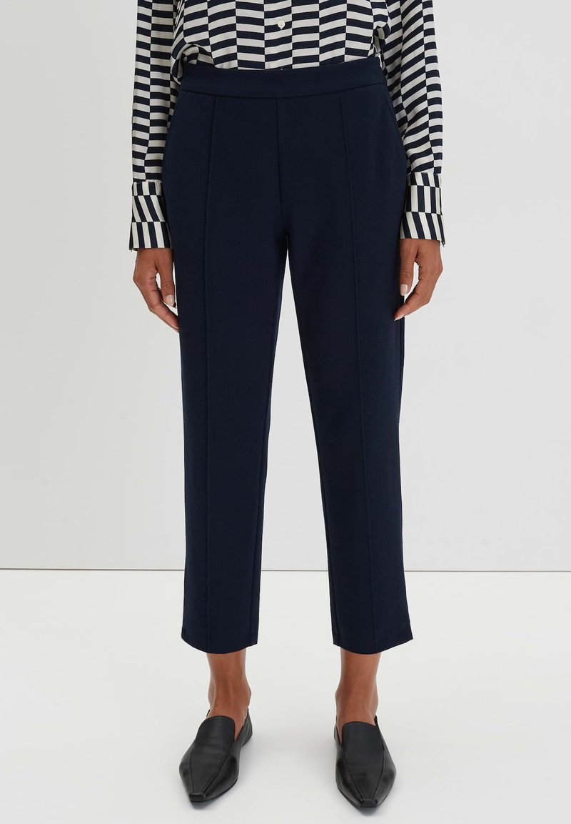 Pantaloni blu scuro sartoriali con vita alta, vestibilità slim e lunghezza cropped, abbinati a una camicia con colletto a righe bianche e nere.
