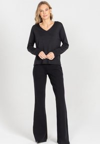 Czarny sweter dzianinowy z dekoltem w serek i prążkowanymi mankietami, zestawiony z czarnymi spodniami dzwonami, tworząc monochromatyczny strój. Gładka tekstura całości.