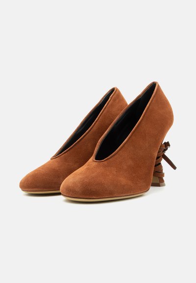 Ζευγάρι καφέ σουέντ γόβες με ψηλό τακούνι, στρογγυλεμένες μύτες και διακοσμητικό φιόγκο στο πίσω μέρος των τακουνιών.
