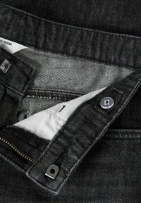 Cintura de jeans de mezclilla negra parcialmente abierta que muestra el botón, ojal, cremallera y tela interior blanca con etiqueta de talla "12Y".