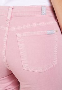 Jeans in denim rosa con un design aderente, caratterizzati da una tasca sul retro e un piccolo logo cucito sopra la linea della vita.
