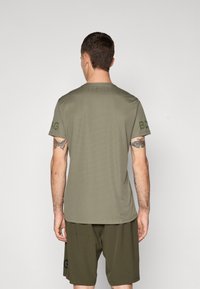 Oliven grønn kortermet t-skjorte med ribbet tekstur, rund hals, og logodetalj på ermene, kombinert med matchende shorts.