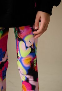 Leggings colorés présentant un motif abstrait vibrant avec des formes en rose, vert, bleu et noir. Le matériau semble extensible avec une texture lisse.