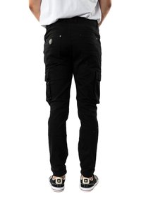 Pantalones cargo negros con múltiples bolsillos y un diseño ajustado. Presenta un cierre de botón y detalles de costura visibles. Se lleva con zapatillas negras.