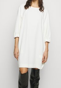 Vit, löst sittande klänning med trekvarts ärm, rundad halsringning och mjuk textur; matchad med svarta stövlar över knäna.