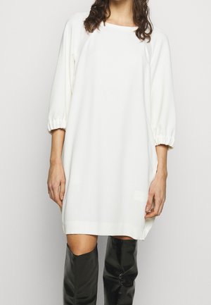 Witte, losvallende jurk met driekwart lange pofmouwen, ronde hals en zachte textuur; gecombineerd met zwarte laarzen tot boven de knie.