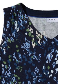 Blouse bleu foncé avec un imprimé floral abstrait bleu, vert et blanc et un col en V avec une étiquette de marque visible.