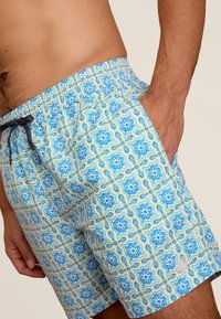 Patronen zwemboxers met blauwe, gele en witte bloemontwerpen, voorzien van een elastische tailleband en een trekkoord voor een verstelbare pasvorm.