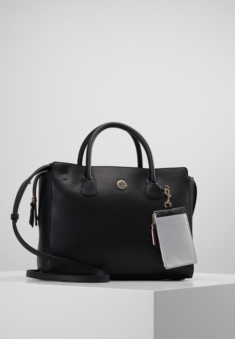Sac à main en cuir noir avec double poignée, bandoulière amovible et un petit porte-cartes gris attaché par un fermoir doré.