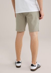 Haki zaļie šorti ar strukturētu apdari, rullētiem malām un klasisku piegriezumu, saskaņoti ar baltām kedām ar melniem akcentiem.