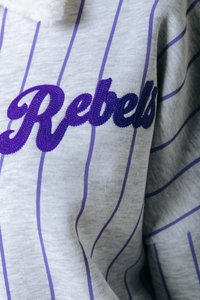 Felpa grigia con strisce verticali viola e logo ricamato "Rebels" in un font stilizzato, con un collo morbido e testurizzato.