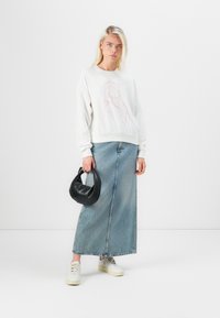 Felpa bianca con disegno a linea rosa, abbinata a una lunga gonna di jeans, sneakers bianche e una borsa nera.