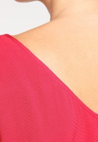 Tissu cramoisi avec une texture lisse, doté d'un large décolleté en V et d'un subtil motif diagonal, mettant en valeur une finition propre sur les bords.