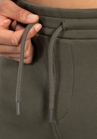 Pantalones de chándal verde oliva con una cinturilla ajustable, con una textura acanalada y extremos de cuerdas oscuros en los cordones.