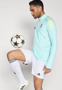 Ilgos rankovės sportinė viršutinė dalis mėtų žalia spalva su juodais akcentais, derinama su baltais šortais ir dryžuotomis kojinėmis. Kamuolio paviršiuje yra žvaigždžių raštai juodos ir rožinės spalvos.