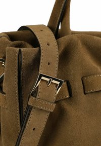 Dettaglio di borsa in camoscio marrone. Presenta una texture liscia e morbida, accessori in metallo e una cinghia con fibbia e dettagli cuciti.