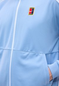 Lichtblauw jack met ritssluiting, geribbelde manchetten, hand in zijzak en een klein meerkleurig Nike-logo op de borst.