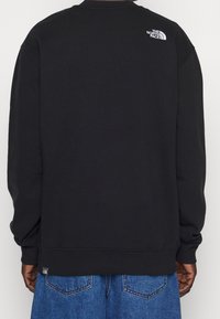 Musta collegepaita, jossa on resoroitu pyöreä kaulus ja hihansuut. Yläselässä pieni valkoinen logo ja rento istuvuus, yhdistetty farkkuihin.