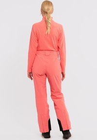 Koraal fleece pullover en bijpassende broek met zwarte accenten en ritssluitingen bij de enkels, met een strakke silhouet en gladde textuur.