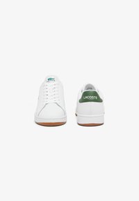 Witte leren sneakers met een gladde textuur, groene accenten bij de hak en een rubberen zool. Kenmerken zijn een vetersluiting aan de voorkant en het logo op de tong en de hak.
