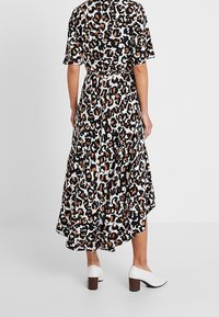 Klänning med leopardmönster, korta ärmar, midjebälte och hög-låg fåll. Vita klackskor med blockklackar kompletterar outfiten.