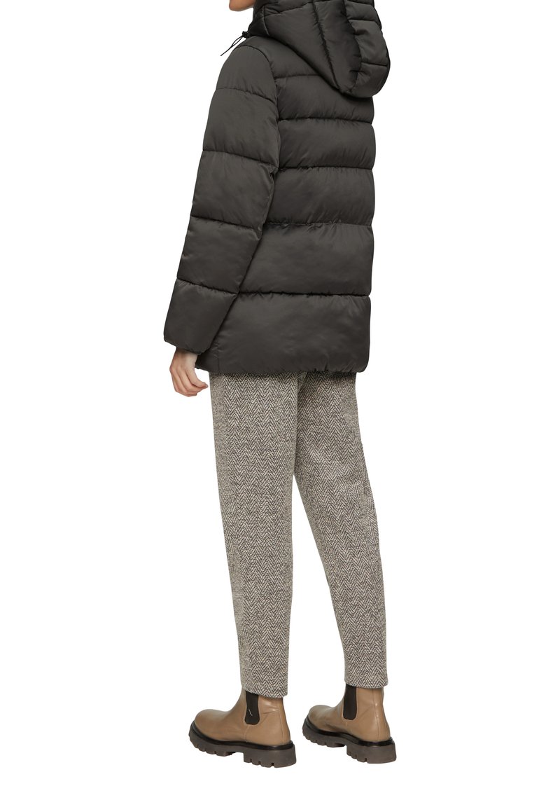 Czarna kurtka puchowa z kapturem, z pikowanym wzorem. Szare spodnie w jodełkę oraz beżowe botki za kostkę dopełniają stylizację.
