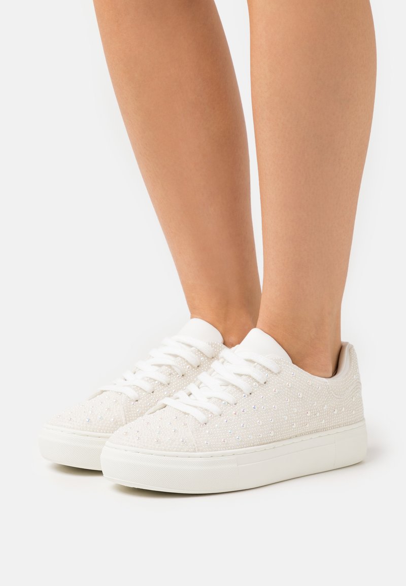 Sneaker bianche in tela con parte superiore testurizzata e piccoli dettagli iridescenti, punta rotonda e suola in gomma. I lacci sono bianchi senza elementi metallici.