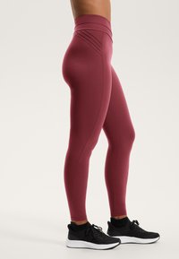 Hoge taille bordeaux leggings met een soepele textuur en accent stikdetails, gecombineerd met zwarte sportschoenen met een witte zool.