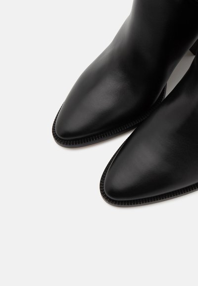Stivaletti neri in pelle con punta affusolata, texture liscia e delicati dettagli a righe lungo i bordi della suola.