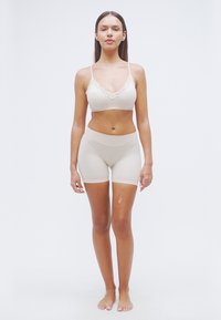 Soutien-gorge sans couture couleur nude avec bordure en dentelle et shorty taille haute assorti. Texture lisse, design ajusté et détails de couture minimaux.