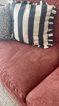 Divano in tessuto rosso con due cuscini decorativi, uno a righe bianche e nere con bordi arricciati, l'altro grigio con un motivo a stampa leopardata.