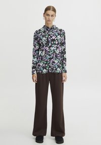 Floral blouse with long sleeves, featuring a black background and multicolored floral pattern; paired with brown wide-leg trousers.