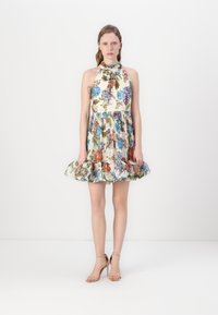 Robe dos nu florale en crème avec des fleurs multicolores. Jupe évasée avec un ourlet à volants. Sandales à talons hauts beiges. Fond minimaliste.