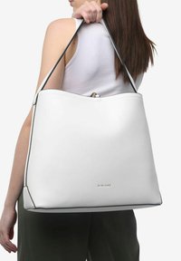 Borsa a tote in pelle bianca con dettagli neri, forma arrotondata e logo in basso. Presenta una singola tracolla.