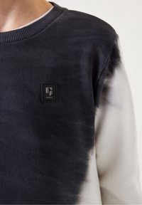 Schwarz-weißer Batik-Sweatshirt aus strukturiertem Stoff. Mit Rundhalsausschnitt, gerippten Bündchen und einem kleinen schwarzen Markenlogo auf der Brust.