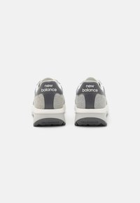 Des baskets New Balance avec un schéma de couleurs gris et blanc, comprenant des matériaux en daim et en mesh, des semelles rembourrées et des accents de logo au niveau du talon.