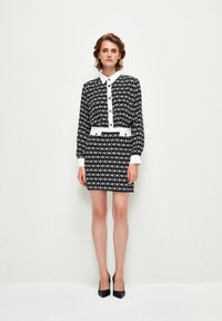 Black and white patterned dress with a collared top, buttons, and a fitted skirt. Features a white belt accent. Smooth texture and tailored fit.