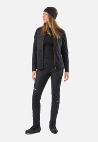 Giacca e pantaloni sportivi neri con texture trapuntata su parte superiore del corpo e cosce. Presentano dettagli con cerniere arancioni e una fascia per capelli.