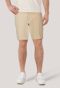 Beige shorts i bomullsmix, med rak skärning, framfickor och midjeband. Bärs med en ljus t-shirt och vita sneakers.